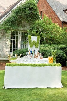 an outdoor bar set up with wine glasses, fruit and bottles on the table in front of a house