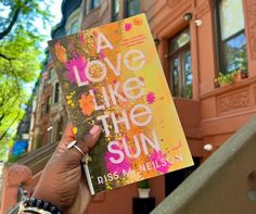 a person holding up a book that says love like the sun in front of a building