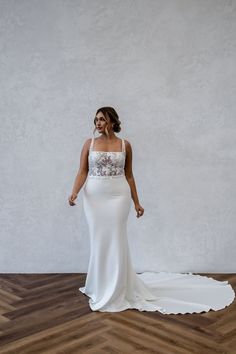 a woman in a white wedding dress standing on a wooden floor with her arms behind her back