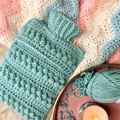 two knitted mittens and a candle on a plate next to some yarns