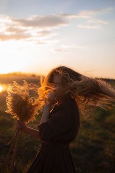 a woman with her hair blowing in the wind, holding a bunch of dried flowers