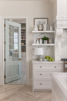 a white kitchen with marble counter tops and open shelving unit next to the door