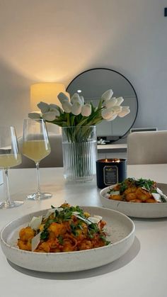 two white plates with food and wine on a table in front of a vase filled with tulips