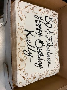 a cake with white frosting and black writing on it sitting in a cardboard box