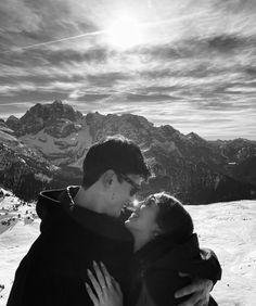 a man and woman embracing each other in the snow with mountains in the back ground