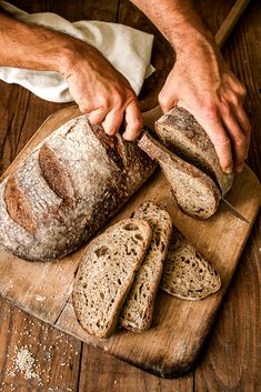 a person cutting bread on top of a wooden board