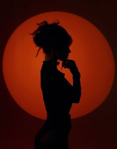 the silhouette of a woman in front of an orange sun with her hair blowing back