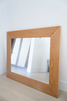 a large wooden mirror sitting on top of a hard wood floor next to a white wall