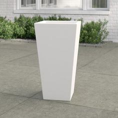 a tall white vase sitting on top of a cement floor next to a building with windows