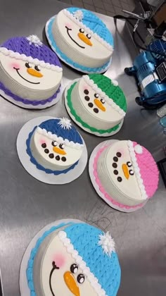 six frosted cakes are arranged in the shape of snowmen on a conveyor belt