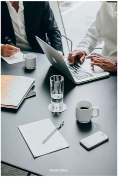 three people sitting at a table with laptops and notebooks on top of it