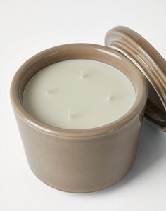 a white candle in a brown container on a white surface with the lid open to show it's contents