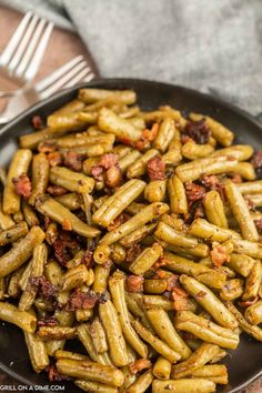 a black plate filled with green beans and bacon on top of a wooden table next to silverware