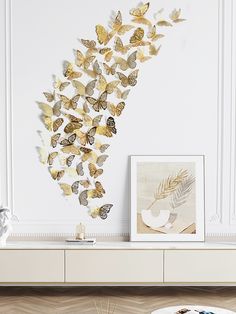 a white table topped with a vase filled with flowers next to a wall covered in gold butterflies