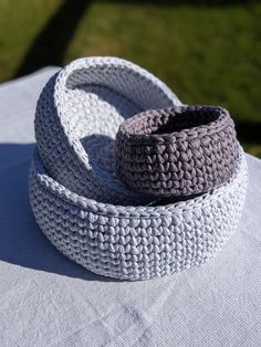 two crocheted baskets sitting on top of a white cloth covered table with grass in the background