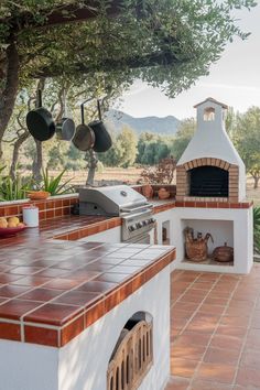 an outdoor grill with pots and pans hanging from it's roof, next to a tree