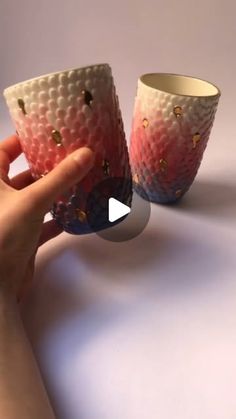 two cups with gold dots on them are being held by someone's hand over a white surface