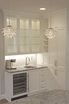 an empty kitchen with white cabinets and marble counter tops, lights hanging from the ceiling