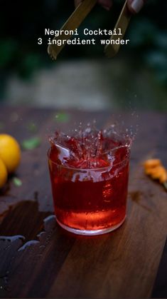 a glass filled with liquid sitting on top of a wooden table next to lemons