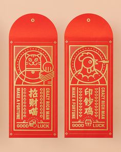 two red and gold paper tags with chinese writing on them, one has an image of a cat