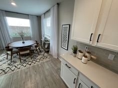 a kitchen and dining room with white cabinets, wood flooring and gray tile on the walls