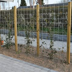 the fence is made of metal wire and has plants growing on it, along with brick pavers