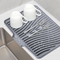 two mugs are sitting on the drainer in the sink next to utensils