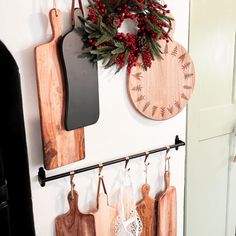 several wooden cutting boards hanging on the wall next to a wreath and other kitchen utensils