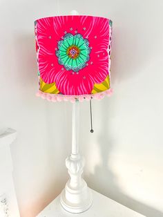 a pink and green lamp shade sitting on top of a white table next to a wall