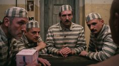 three men in prison uniforms are sitting at a table and one is holding a box