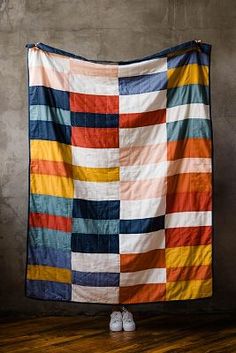 a large multicolored quilt hanging on the wall in front of a pair of white shoes