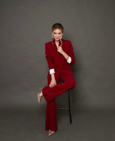 a woman in a red suit is sitting on a chair and posing for the camera