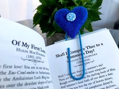 an open book with a blue heart hanging from it's cover, next to a potted plant