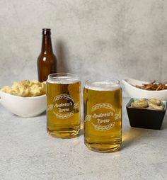 two glasses filled with beer sitting on top of a table next to bowls of food