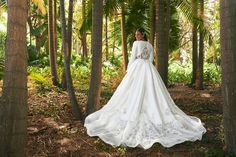 a woman is standing in the woods wearing a wedding dress with long sleeves and an open back