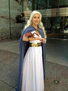 a woman dressed in white and blue is standing on the sidewalk with her arms crossed