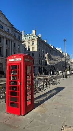 a red phone booth sitting on the side of a road next to bicycles and buildings