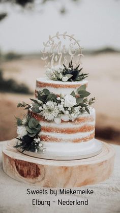 a wedding cake with flowers and greenery on top