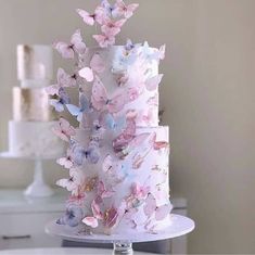 a three tiered cake with pink and blue butterflies on it sitting on a table