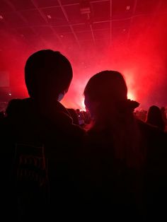 two people standing next to each other in front of red and white lights at a concert