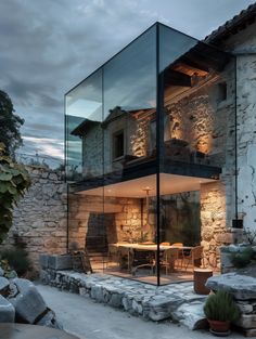 a glass walled house with an outdoor dining area in the front and side walls that are made out of stone