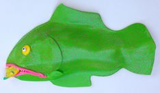 a green plastic fish with yellow eyes on it's face and mouth, sitting on a white surface