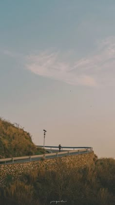 two people are standing on the side of a hill looking at something in the distance