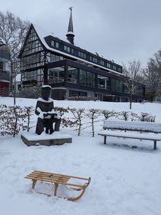 a snow covered park bench sitting next to a statue in front of a large building