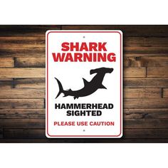 a shark warning sign is hanging on a wooden wall with planks in the background