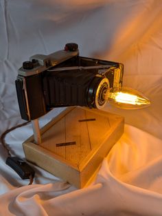 an old fashioned camera sitting on top of a wooden box next to a light bulb