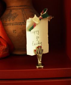 a hand is holding a piece of paper that says happy go lucky on it, next to a vase