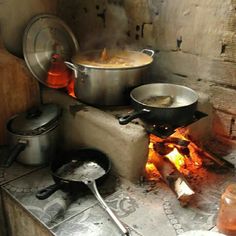 pots and pans are cooking over an open fire in a kitchen with brick walls