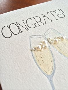 congratulations card with two champagne glasses and pearls on the bottom, sitting on a wooden table