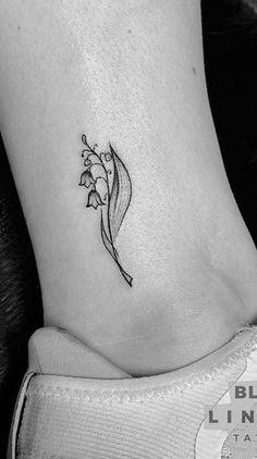 a black and white photo of a small flower on the ankle tattoo by blue line tattoos